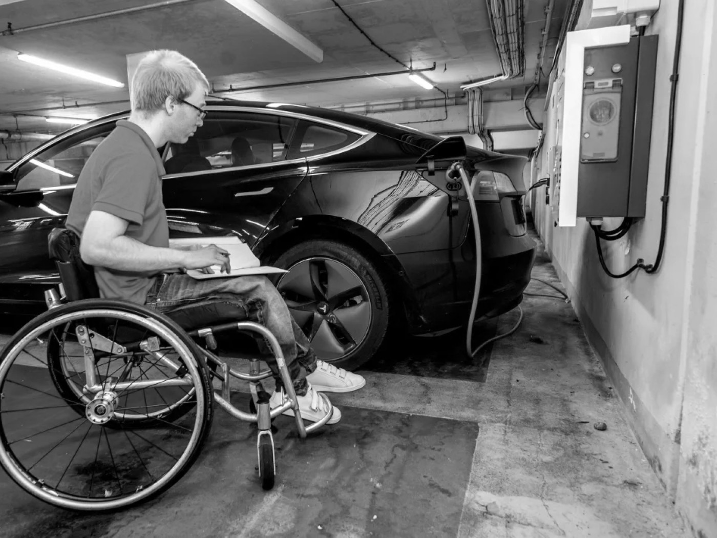 A wheelchair user charging an electric car at an accessible parking bay
